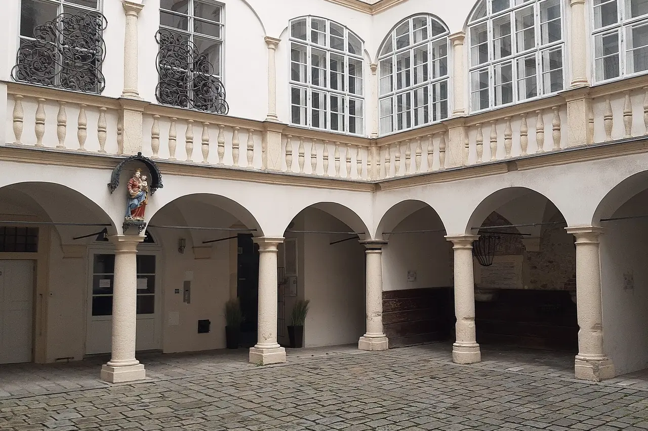 Innenhof eines historischen Wiener Gebäudes mit Arkaden, Säulen und hohen Sprossenfenstern